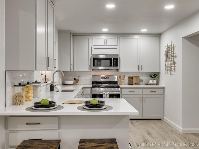 kitchen with appliances with stainless steel finishes, light countertops, backsplash, light wood finished floors, and a sink