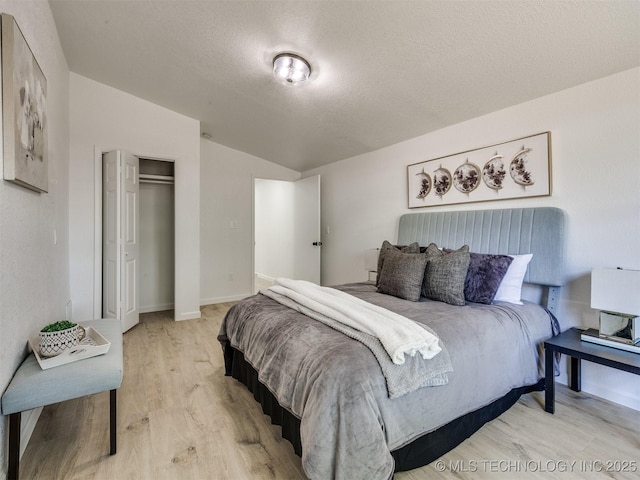 bedroom featuring a closet, vaulted ceiling, light wood finished floors, baseboards, and a textured ceiling