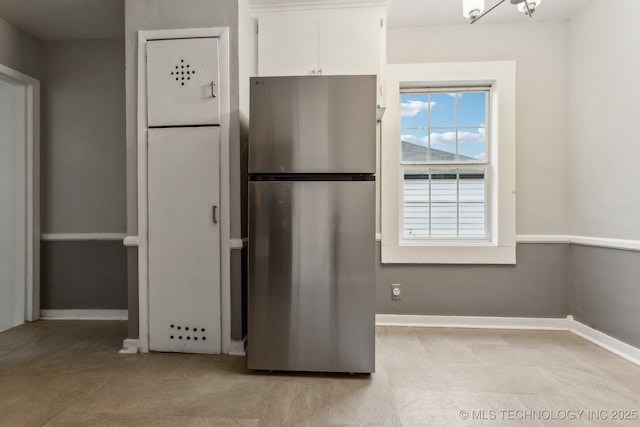 kitchen featuring freestanding refrigerator, white cabinets, and baseboards