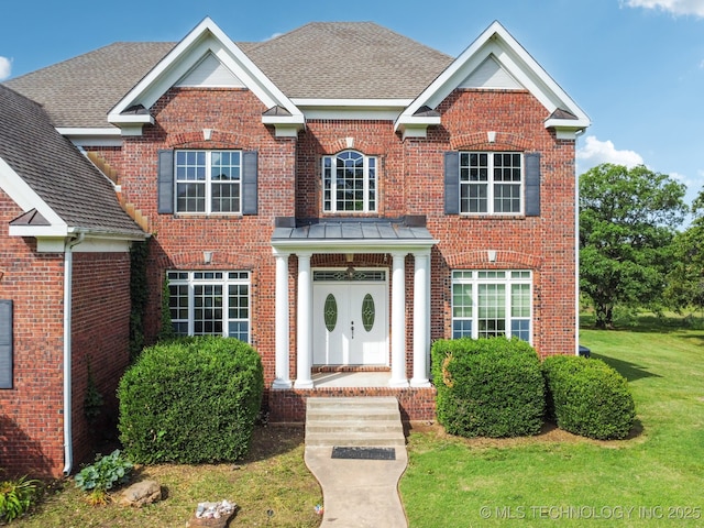 view of front of home with a shingled roof, brick siding, and a front lawn