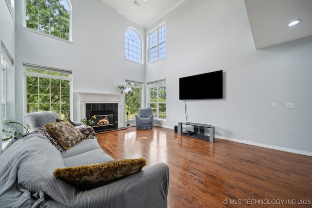 living room with a tile fireplace, high vaulted ceiling, wood finished floors, and baseboards