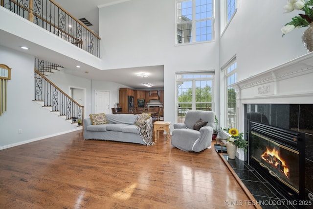 living room featuring a tiled fireplace, wood finished floors, stairs, baseboards, and a high ceiling