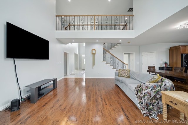living room featuring a towering ceiling, wood finished floors, stairway, and baseboards