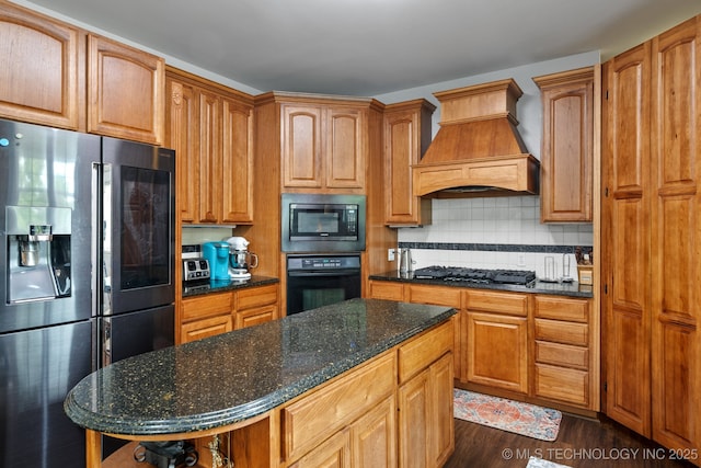 kitchen featuring dark wood finished floors, custom exhaust hood, dark stone counters, black appliances, and backsplash