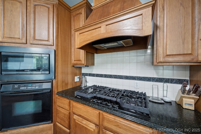 kitchen featuring dark stone countertops, decorative backsplash, brown cabinetry, custom range hood, and black appliances