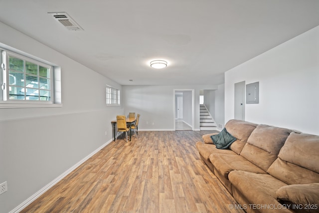 living room with visible vents, electric panel, baseboards, wood finished floors, and stairs