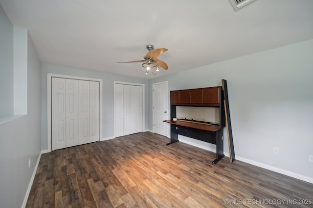 unfurnished bedroom featuring wood finished floors, multiple closets, a ceiling fan, and baseboards