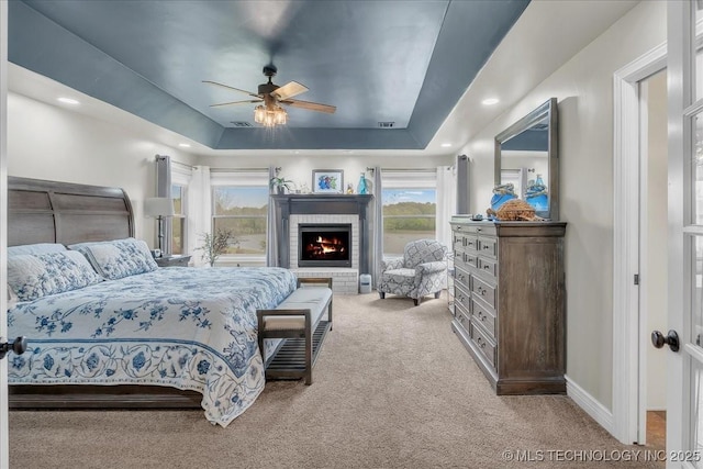 carpeted bedroom with a brick fireplace, baseboards, ceiling fan, recessed lighting, and a tray ceiling