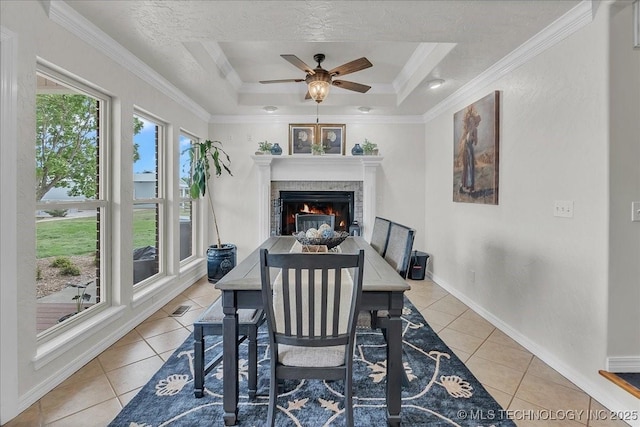 dining area featuring ornamental molding, light tile patterned flooring, a lit fireplace, a raised ceiling, and a ceiling fan