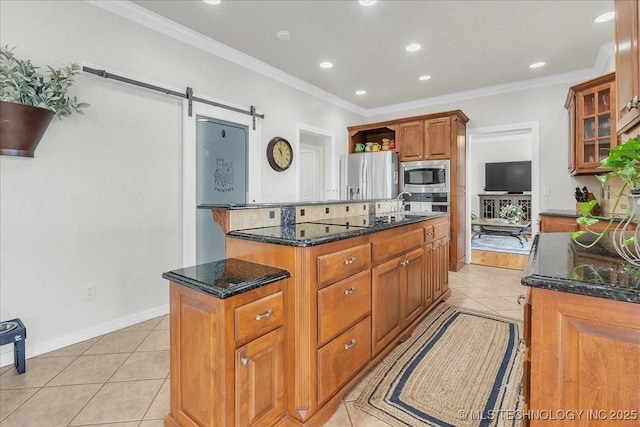 kitchen with crown molding, light tile patterned flooring, an island with sink, dark stone counters, and stainless steel appliances