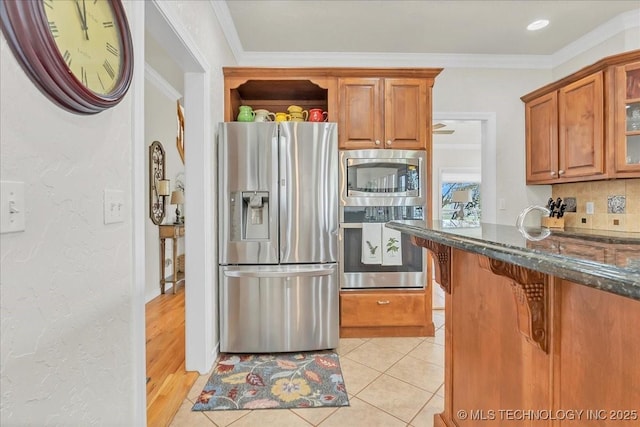 kitchen featuring tasteful backsplash, brown cabinetry, stainless steel appliances, and dark stone countertops