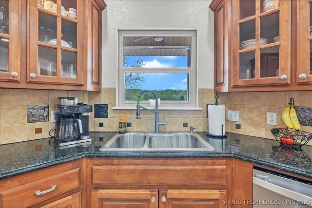 kitchen with brown cabinetry, tasteful backsplash, stainless steel dishwasher, a sink, and glass insert cabinets