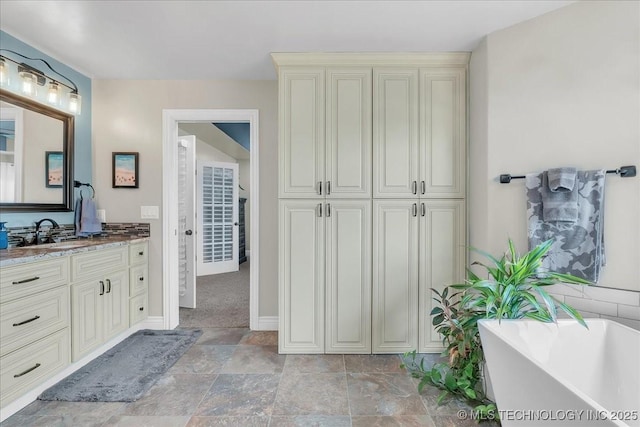 bathroom with vanity, baseboards, a freestanding bath, and stone finish floor