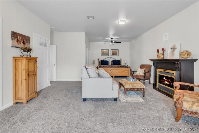 living area featuring visible vents, a glass covered fireplace, baseboards, light colored carpet, and a ceiling fan