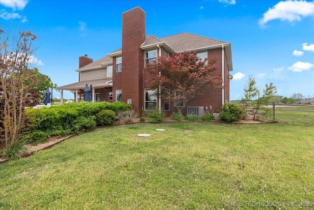 back of house with a lawn, a chimney, fence, and brick siding