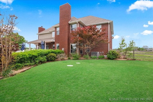 back of house with fence, a chimney, a yard, and brick siding