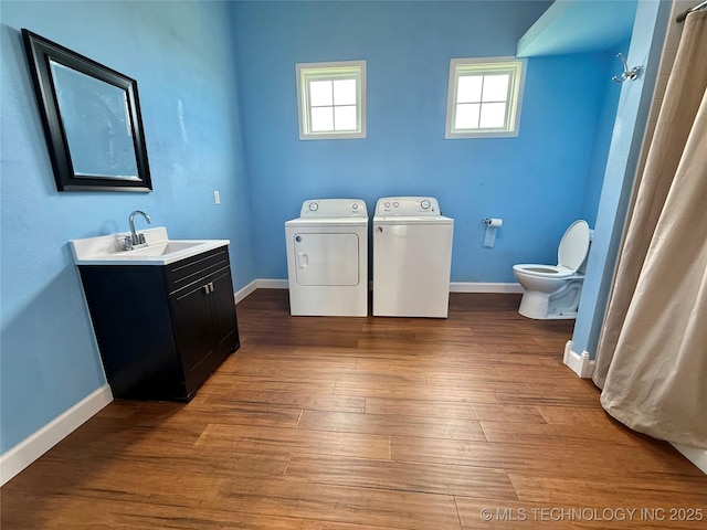 laundry area featuring laundry area, wood finished floors, washer and dryer, baseboards, and a sink