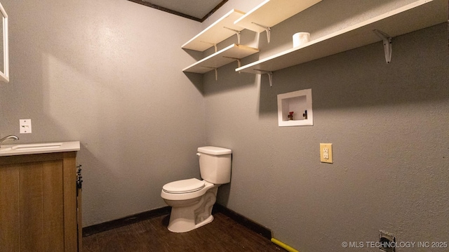bathroom with toilet, vanity, wood finished floors, and baseboards