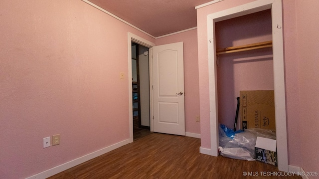 unfurnished bedroom featuring baseboards, crown molding, a closet, and dark wood-type flooring