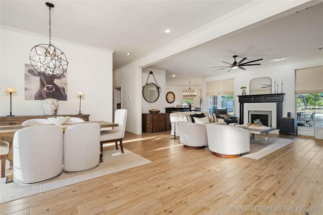 living room with ornamental molding, a fireplace, ceiling fan with notable chandelier, and light wood-style floors