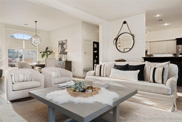 living area featuring visible vents, wood finished floors, ornamental molding, and a notable chandelier