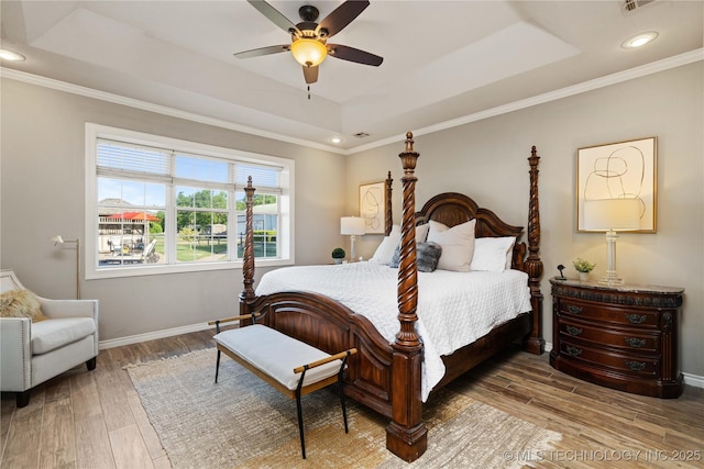 bedroom with wood finished floors, a raised ceiling, crown molding, and baseboards