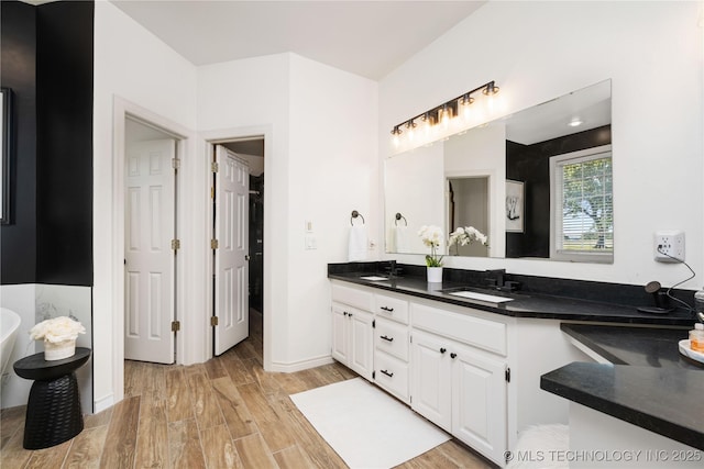 full bathroom with baseboards, wood finished floors, double vanity, and a sink