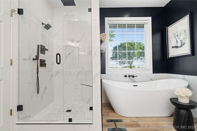 full bathroom with a wealth of natural light, wood finished floors, a freestanding bath, and a marble finish shower