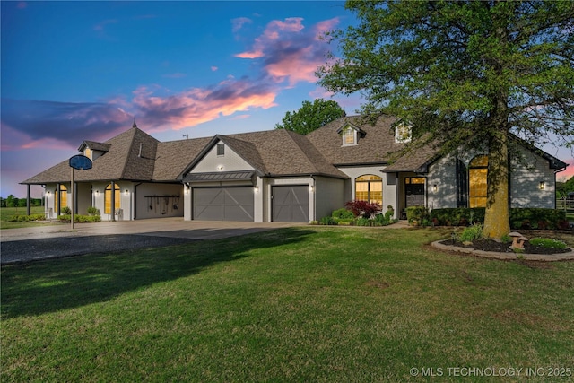 french country style house featuring roof with shingles, driveway, a yard, and an attached garage