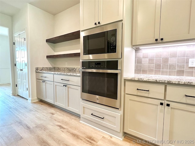kitchen featuring light stone countertops, light wood-style flooring, decorative backsplash, open shelves, and appliances with stainless steel finishes