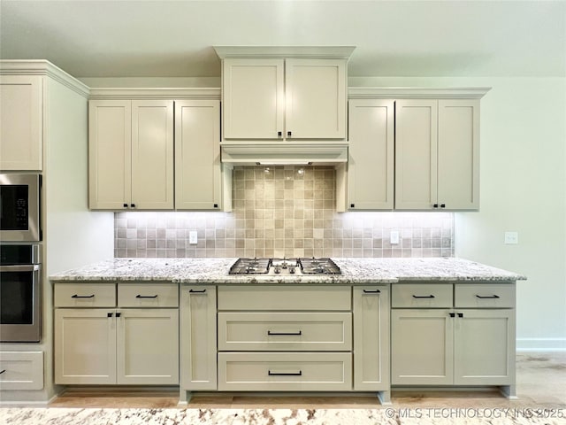 kitchen with light stone countertops, stainless steel appliances, backsplash, and range hood