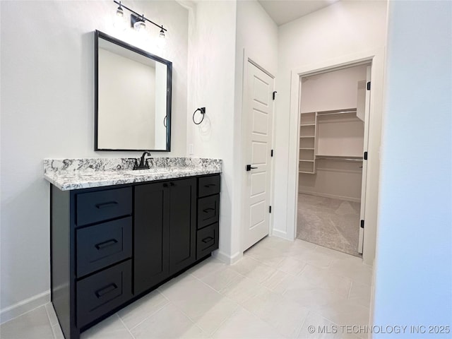 bathroom with a spacious closet, vanity, tile patterned flooring, and baseboards