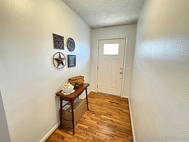 doorway to outside featuring light wood-type flooring, a textured ceiling, and baseboards