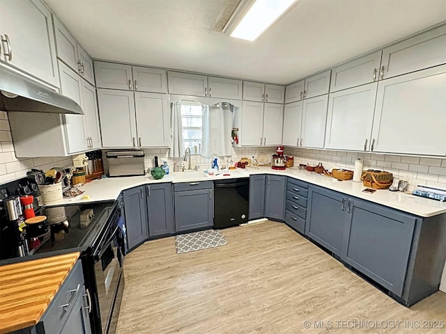 kitchen featuring gray cabinets, light wood finished floors, black appliances, and tasteful backsplash