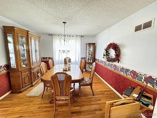 dining room featuring a textured ceiling, visible vents, baseboards, light wood-style floors, and wallpapered walls