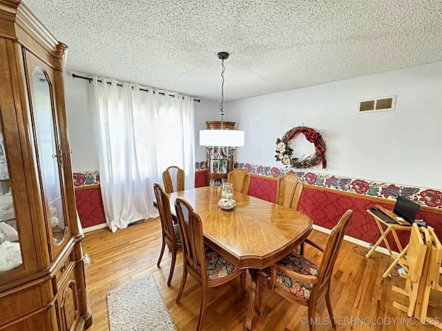 dining area with a textured ceiling, visible vents, baseboards, and light wood-style floors