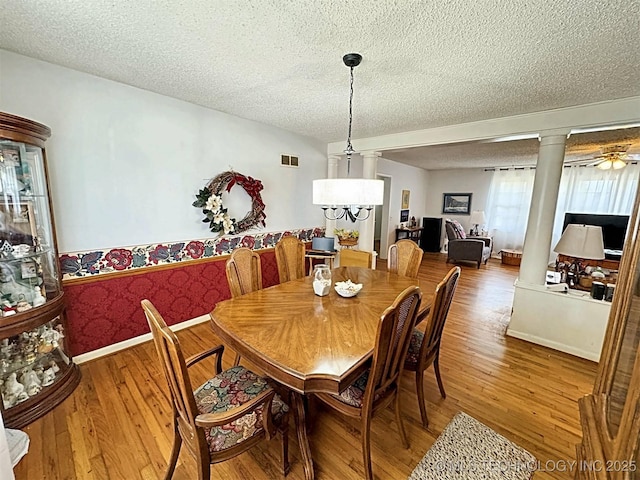 dining room with a textured ceiling, visible vents, baseboards, ornate columns, and hardwood / wood-style floors