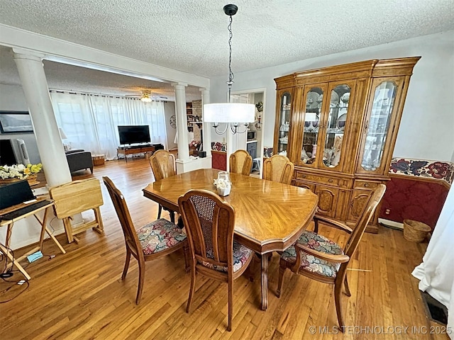 dining space with a textured ceiling, ornate columns, and light wood-style flooring