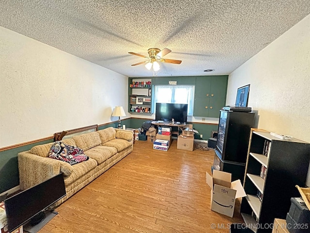 living room with a textured ceiling, a textured wall, a ceiling fan, and wood finished floors