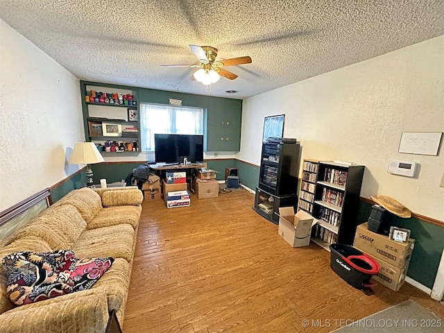 living area featuring a textured ceiling, ceiling fan, wood finished floors, and a textured wall