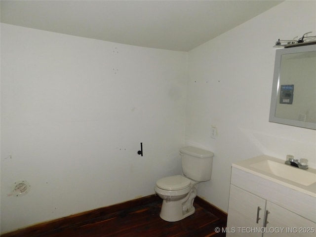 half bathroom featuring toilet, vanity, wood finished floors, and baseboards