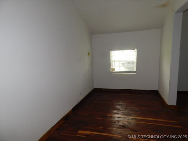 empty room featuring lofted ceiling, wood finished floors, and baseboards