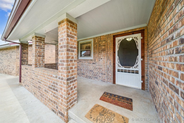 doorway to property with a porch and brick siding
