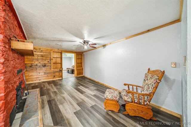 living area featuring baseboards, wood finished floors, ceiling fan, and a textured ceiling