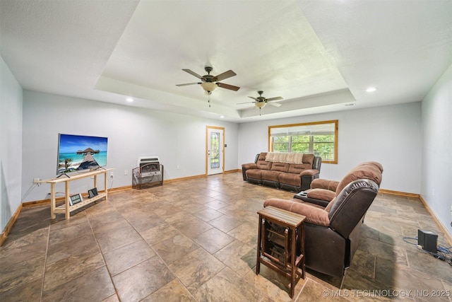 living room featuring recessed lighting, stone finish flooring, baseboards, a raised ceiling, and a ceiling fan
