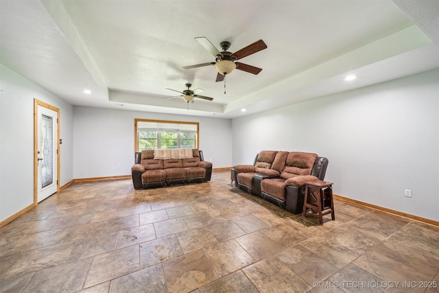 living room with ceiling fan, stone finish floor, a raised ceiling, and baseboards