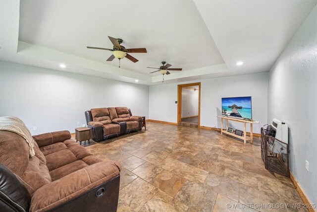 living area with recessed lighting, ceiling fan, stone finish flooring, a tray ceiling, and baseboards