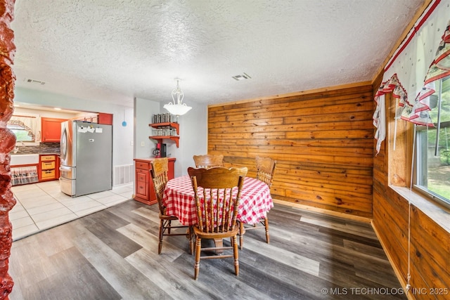 dining area featuring wooden walls, visible vents, light wood-type flooring, and a textured ceiling
