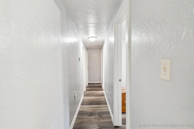 hall featuring wood finished floors, a textured wall, and baseboards