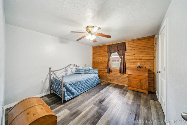 bedroom featuring a textured ceiling, wood walls, ceiling fan, baseboards, and wood finished floors